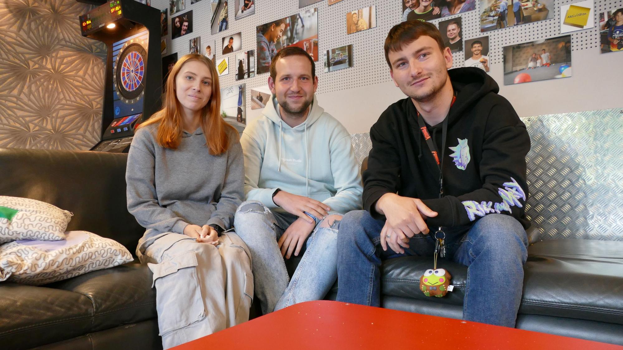 Eine junge Frau und zwei junge Männer sitzen auf einer Couch.