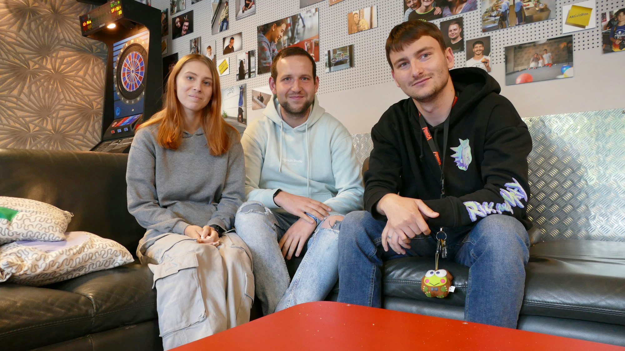 Eine junge Frau und zwei junge Männer sitzen auf einer Couch.