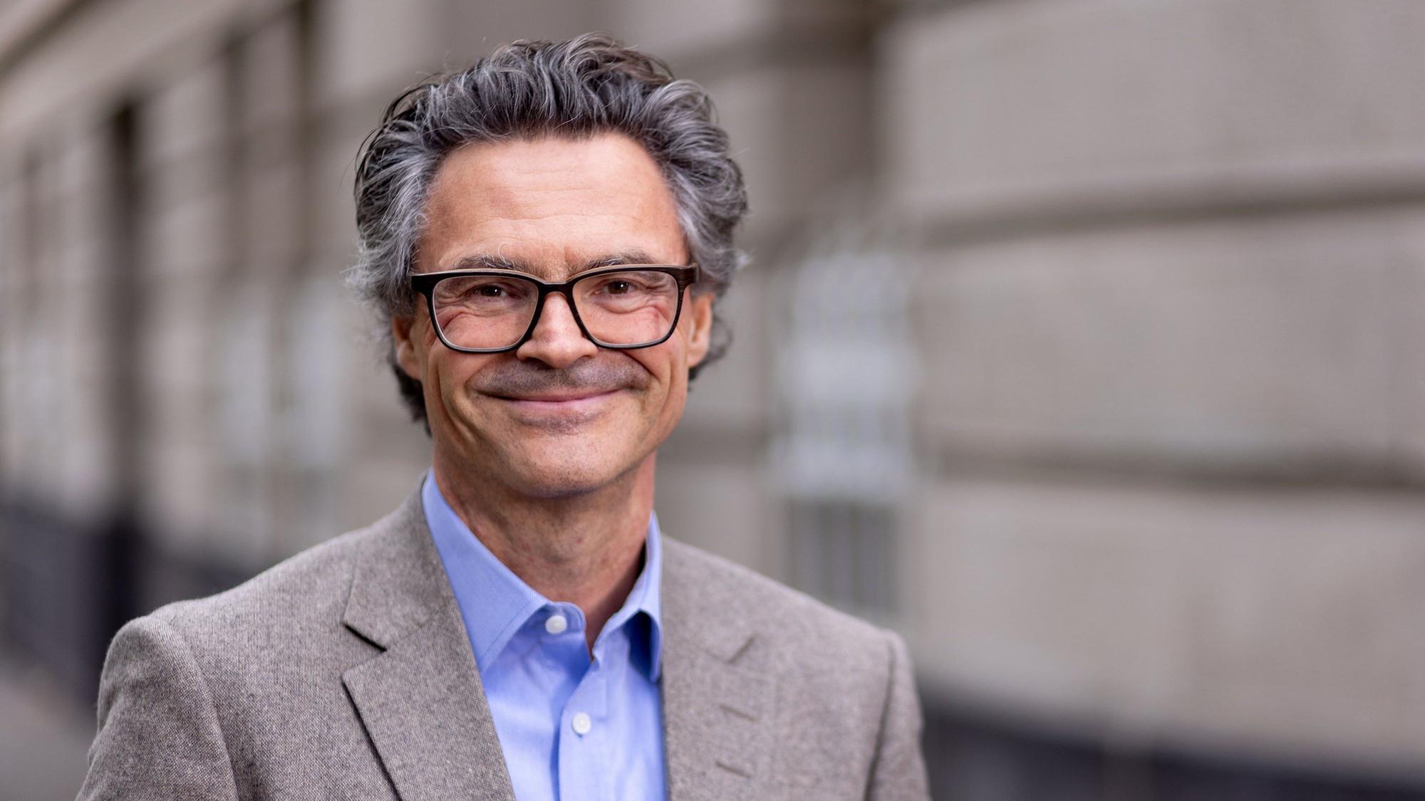 Professor Dr. Rolf Schwartmann trägt einen grauen Anzug und lächelt