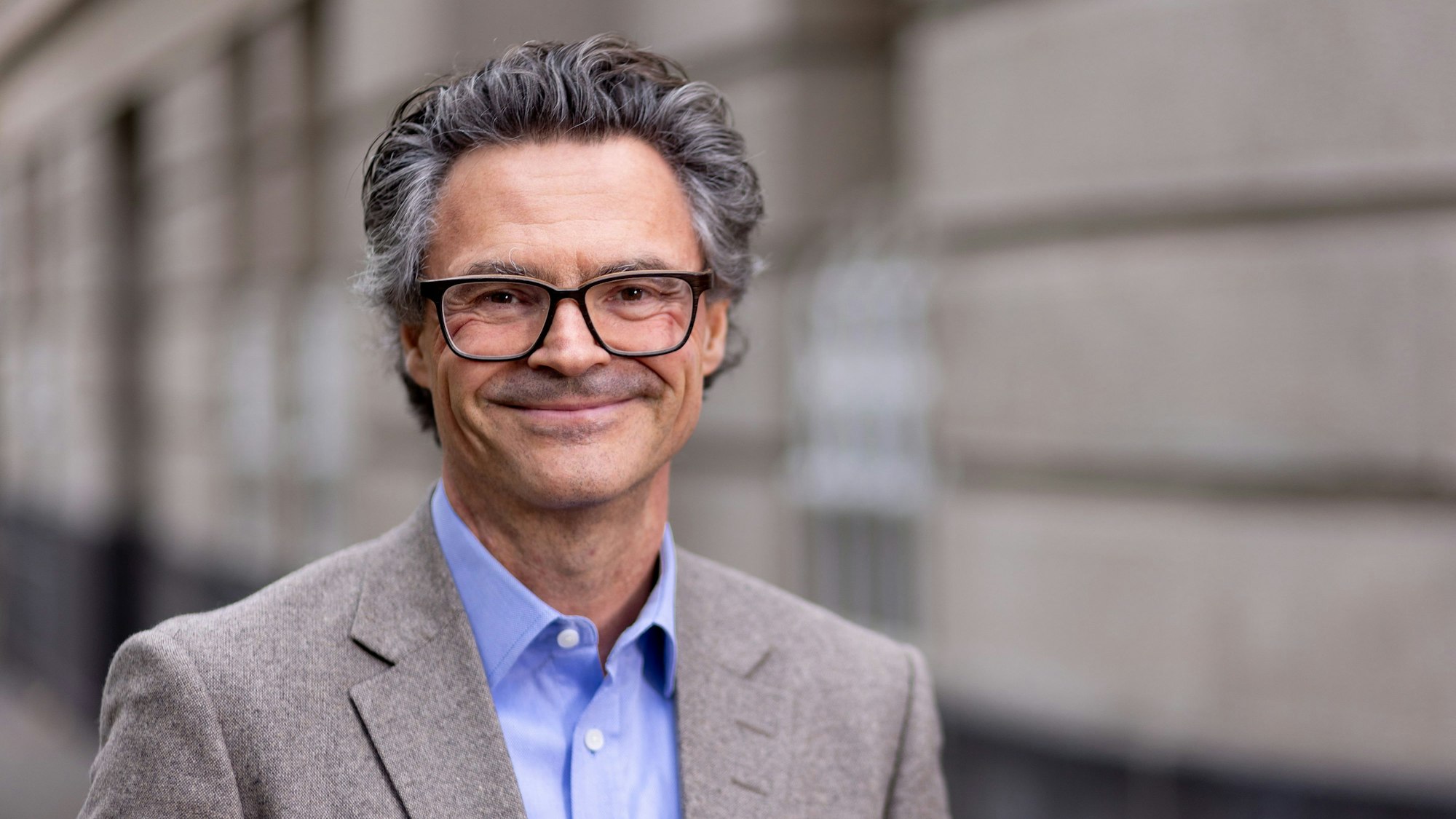 Professor Dr. Rolf Schwartmann trägt einen grauen Anzug und lächelt