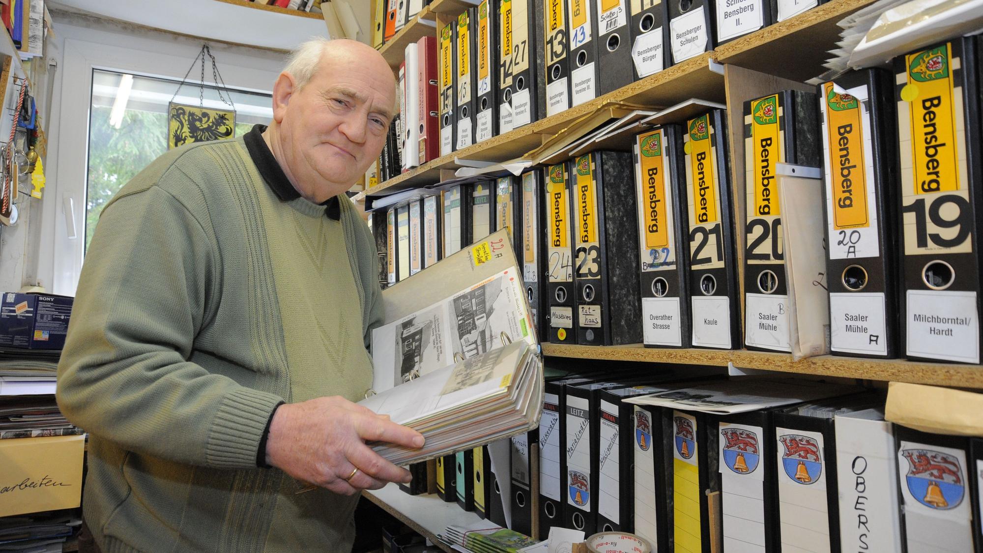 Willi Fritzen steht mit einem Ordner in seinem Archiv,