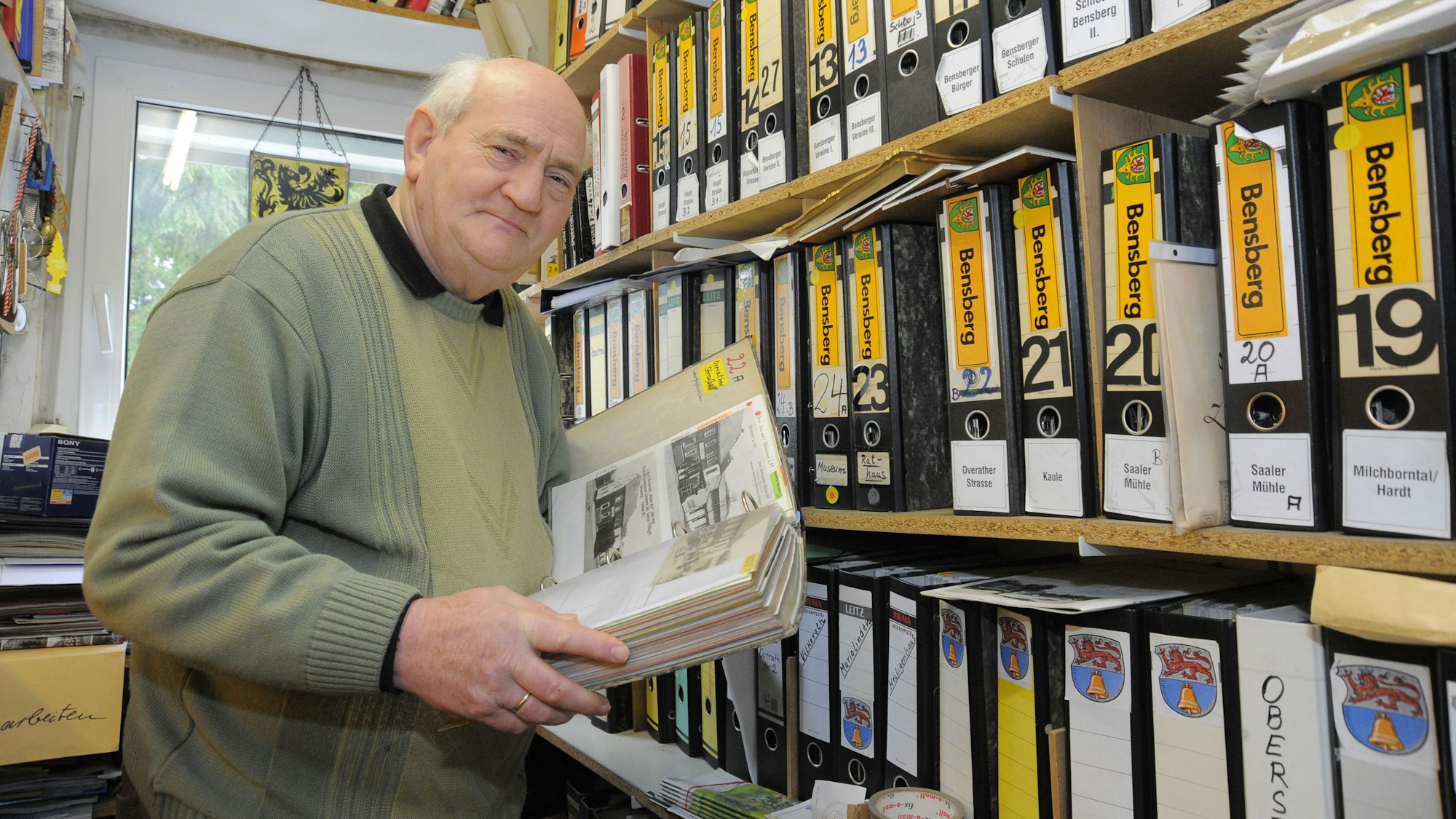 Willi Fritzen steht mit einem Ordner in seinem Archiv,