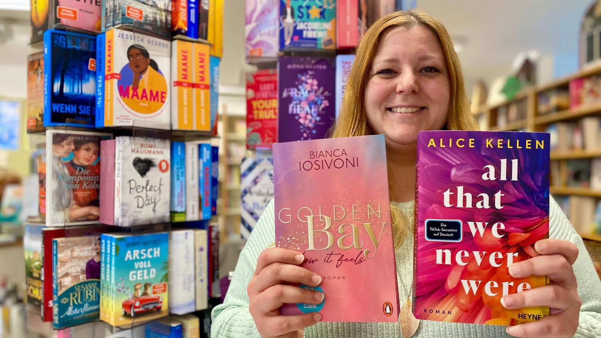 Nora Poschen hält zwei Buchtitel mit goldener und weißer Schrift in die Kamera.
