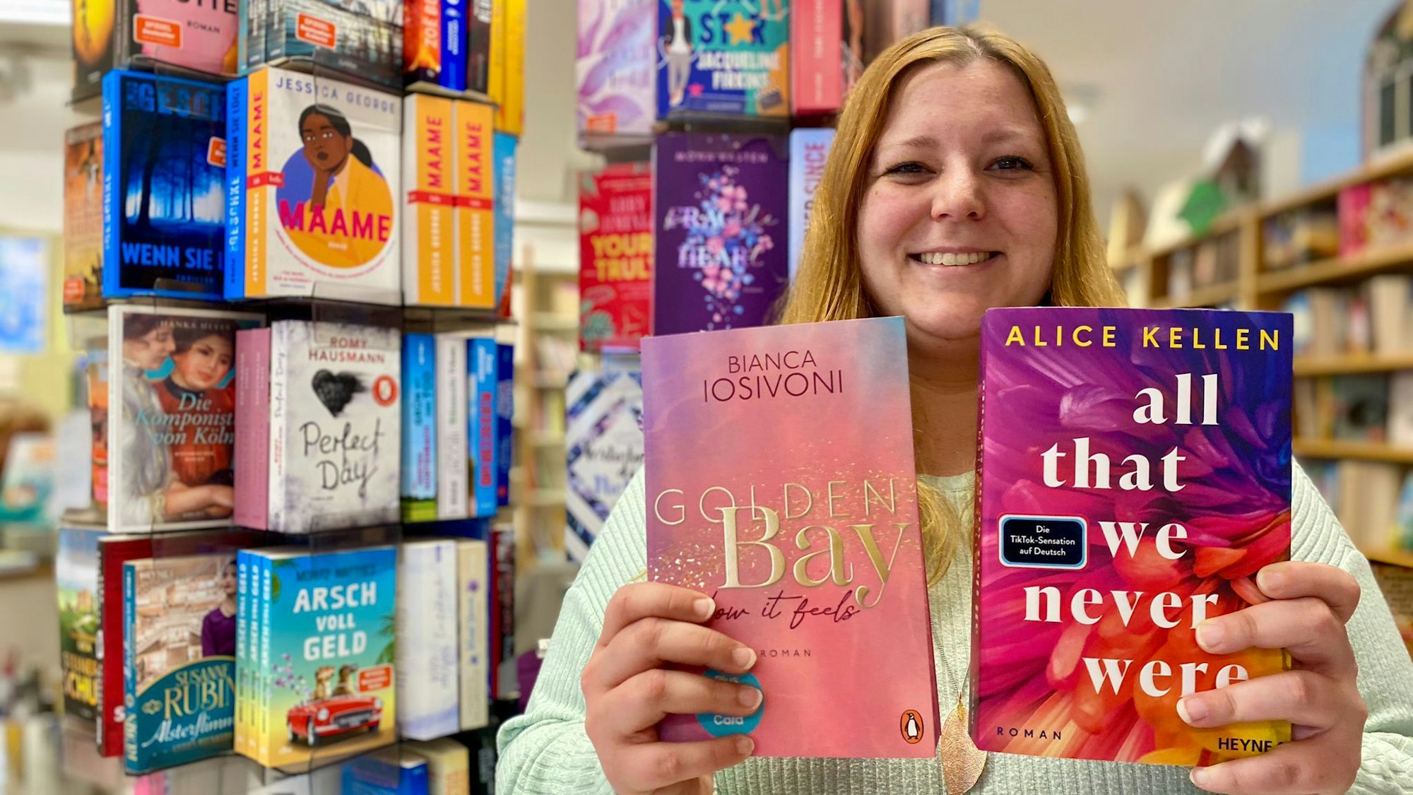 Nora Poschen hält zwei Buchtitel mit goldener und weißer Schrift in die Kamera.