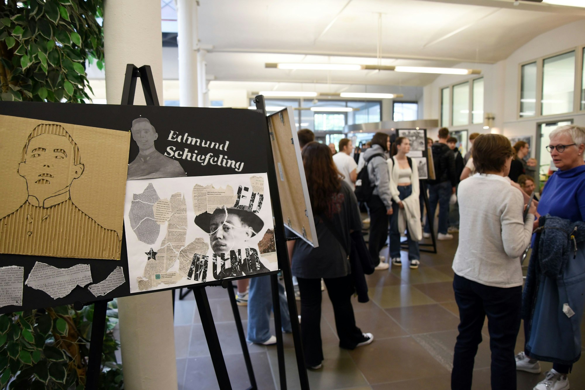 Auf Leinwandständern sind Kunstwerke zu sehen, Menschen stehen zusammen und sprechen.