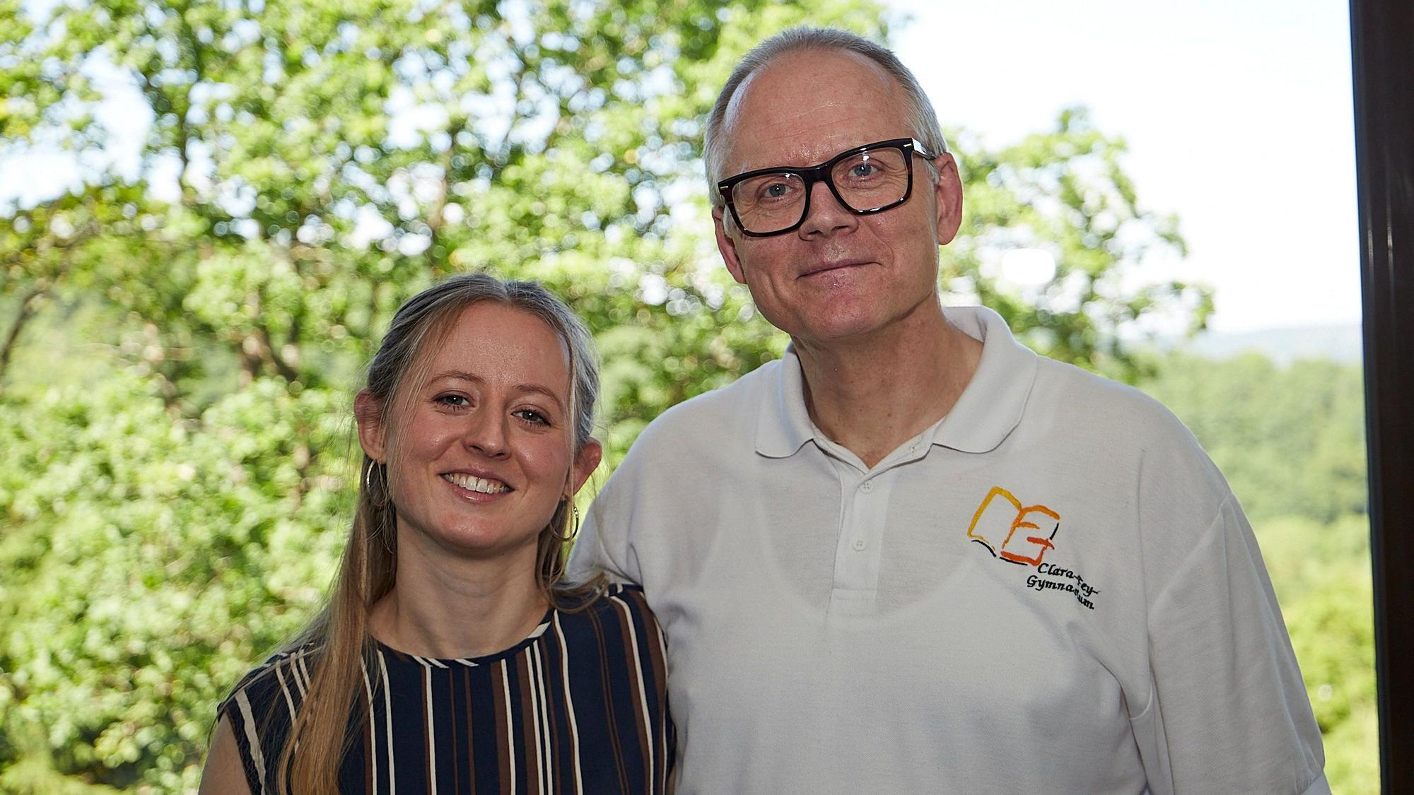 Rudolf Berens und seine Tochter Hannah stehen zusammen vor einem Fenster, im Hintergrund sind grüne Bäume zu sehen.