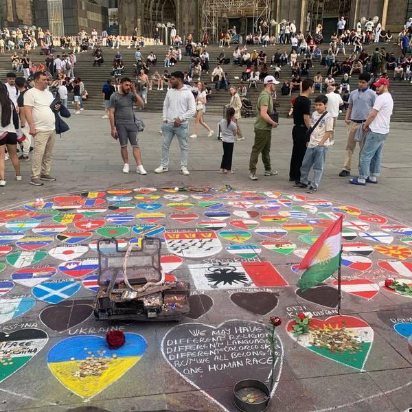 Passanten am Kölner Dom betrachten ein Kreidebild, das die Fahnen vieler Länder zeigt.