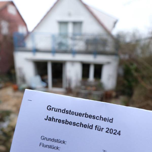 Ein Grundsteuerbescheid wird vor ein unfertiges Haus gehalten.