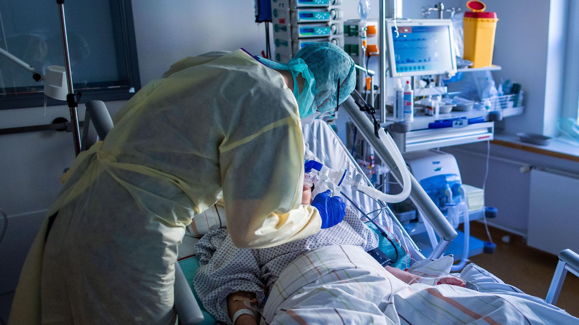 Ein Mitarbeiter richtet bei einer an Covid-19 erkrankten Patientin in einem Zimmer des besonders geschützten Teils der Intensivstation des Universitätsklinikums Greifswald die Beatmungsmaske.