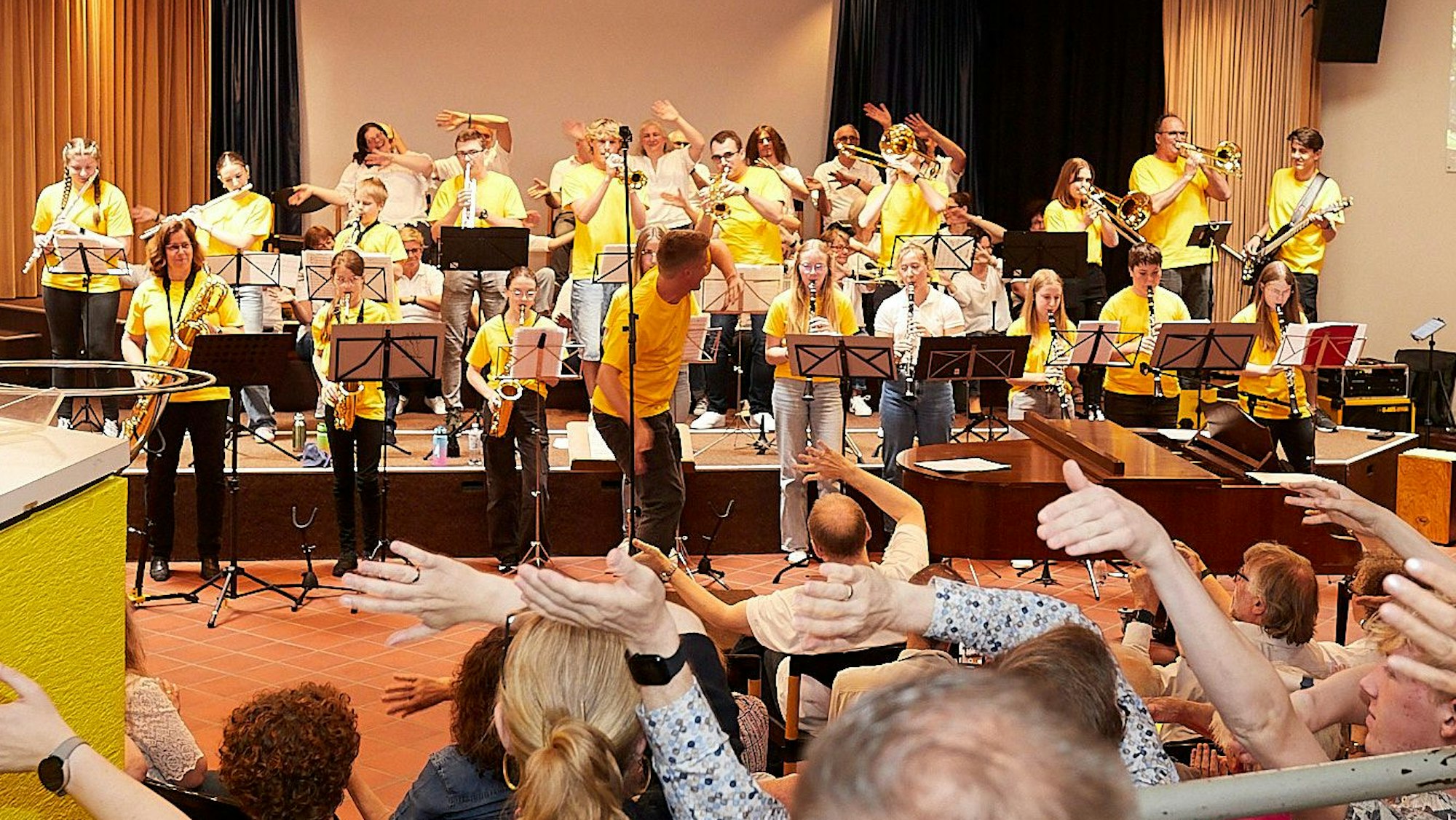 Musiker in gelben Shirts stehen auf der Bühne, das Publikum winkt.