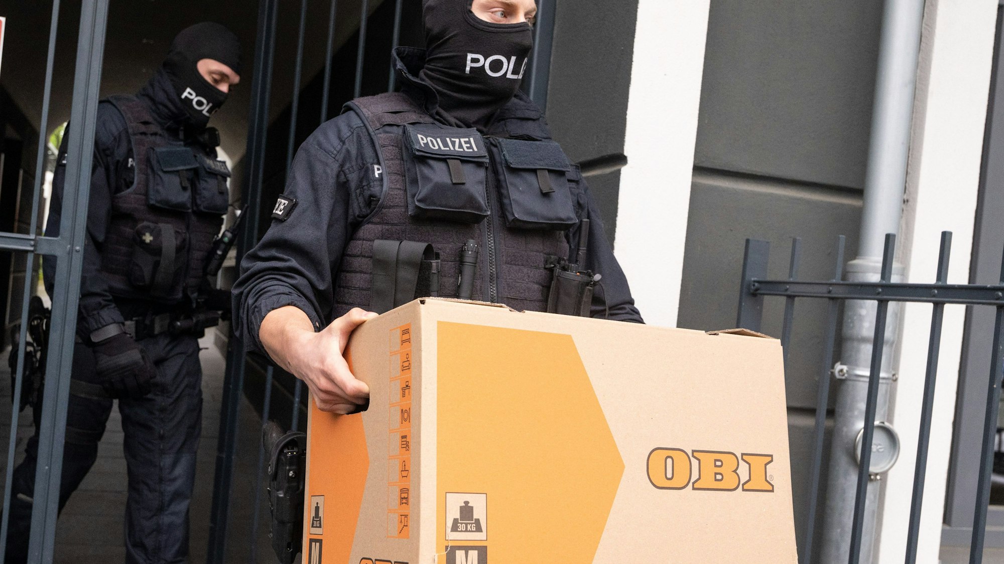 Bonn: Ein Polizist trägt im Rahmen einer Razzia gegen Schleuser einen Karton aus einem Gebäude.