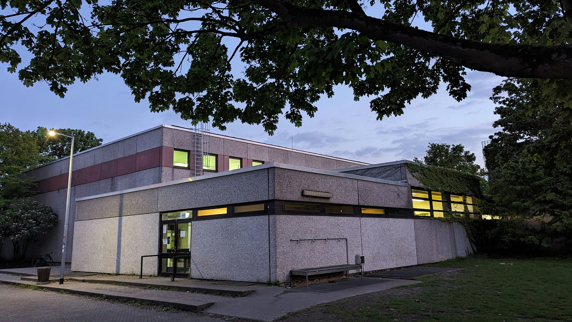 Ein beleuchteter Turnhallenkomplex bei Abenddämmerung.