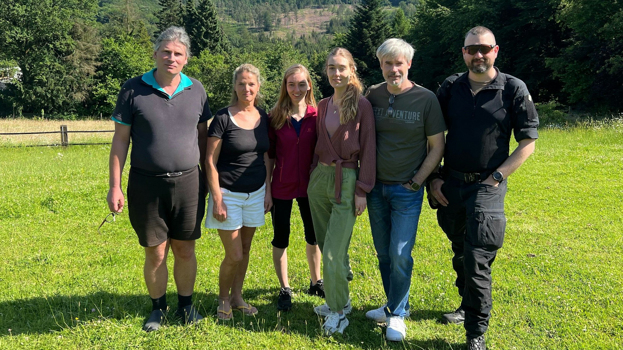 Drei Männer und drei Frauen stehen auf einer Wiese.