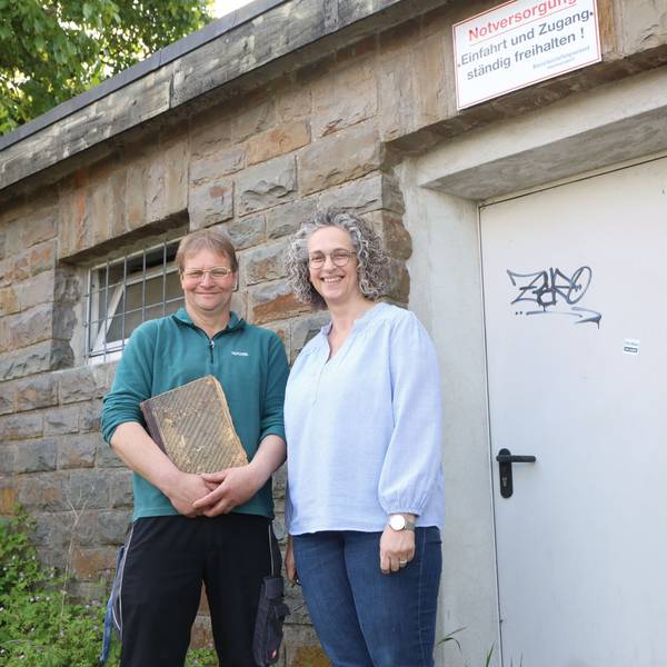 In Waldbröl-Hermesdorf wird der Wasserbeschaffungsverein 125 Jahre alt. Andrea Engelbert und Jürgen Greb stehen an einem Pumpenhaus. Greb hütet dessen altes Protokollbuch wie einen Schatz. Die beiden stehen vor dem Pumpenhäuschen in Hermesdorf.