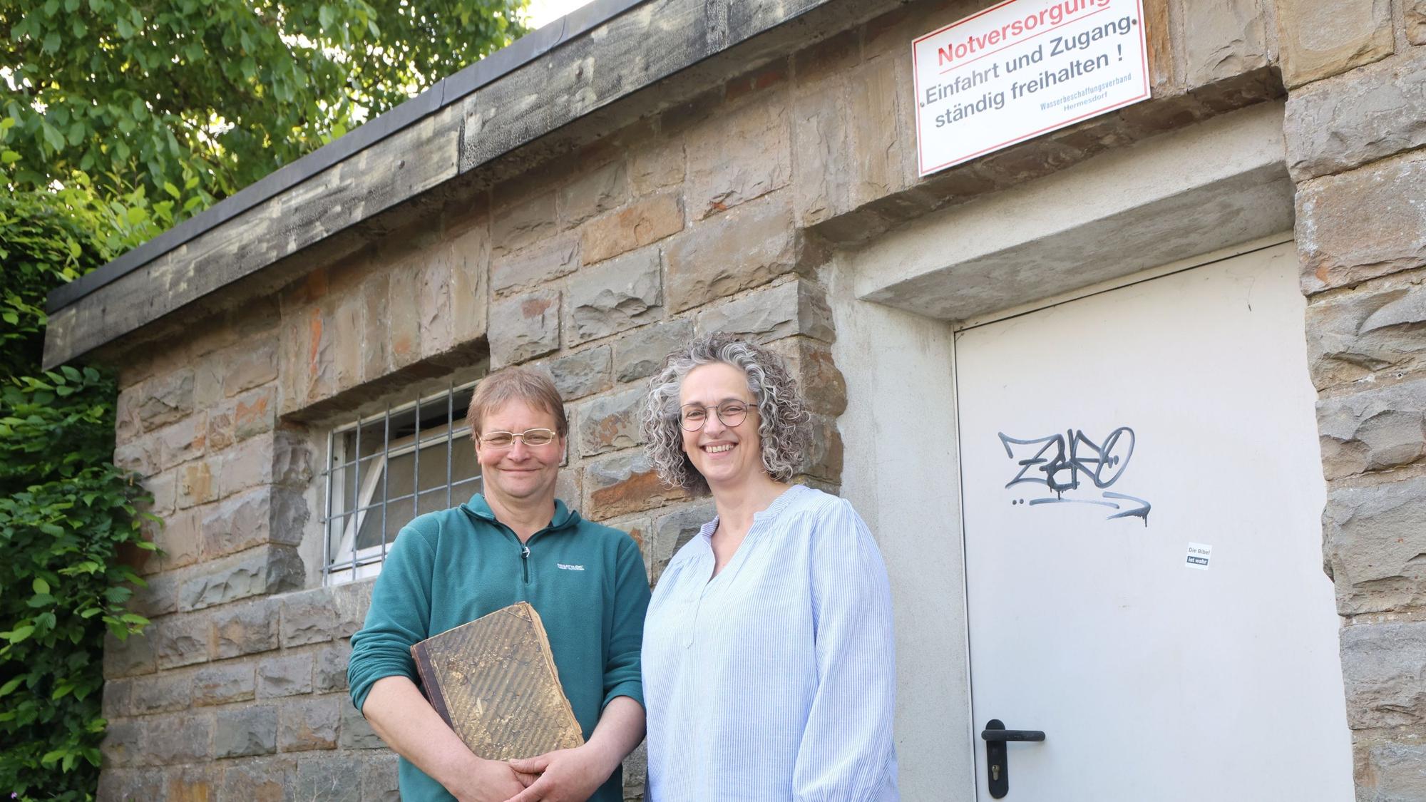 In Waldbröl-Hermesdorf wird der Wasserbeschaffungsverein 125 Jahre alt. Andrea Engelbert und Jürgen Greb stehen an einem Pumpenhaus. Greb hütet dessen altes Protokollbuch wie einen Schatz. Die beiden stehen vor dem Pumpenhäuschen in Hermesdorf.