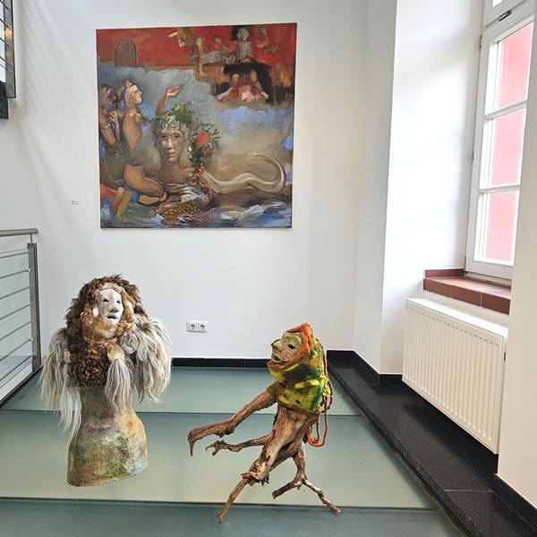 Vor einem Bild mit Lebewesen aus fremden Welten stehen zwei Figuren, die an Geister erinnern.