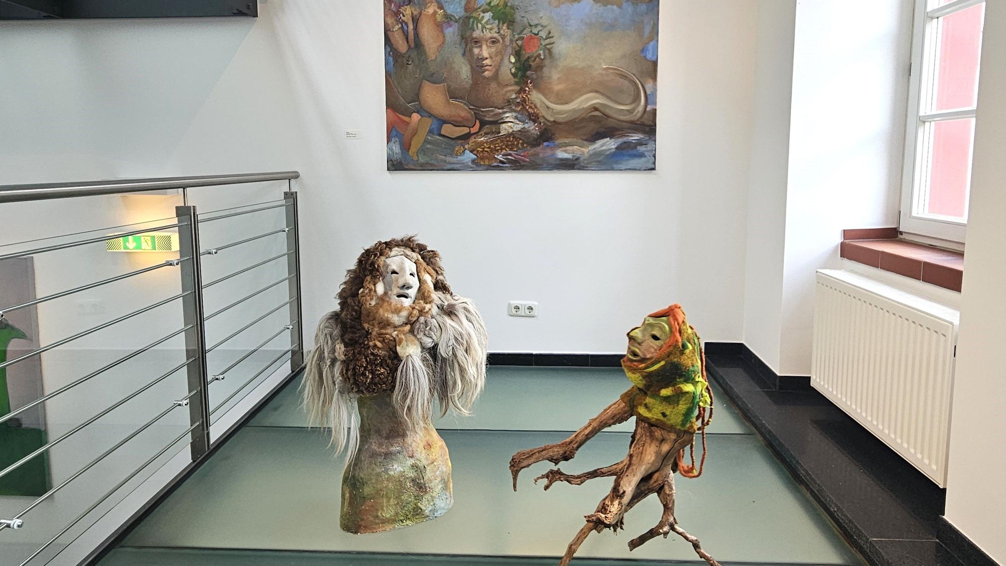 Vor einem Bild mit Lebewesen aus fremden Welten stehen zwei Figuren, die an Geister erinnern.