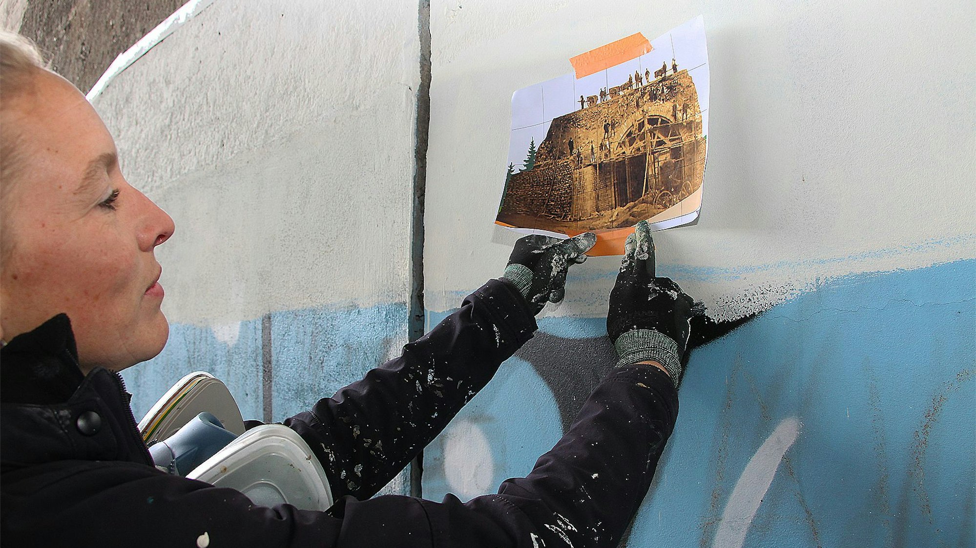 Lena Ortmann hält eine Kopie des alten Schwarz-Weiß-Fotos auf die Betonwand.