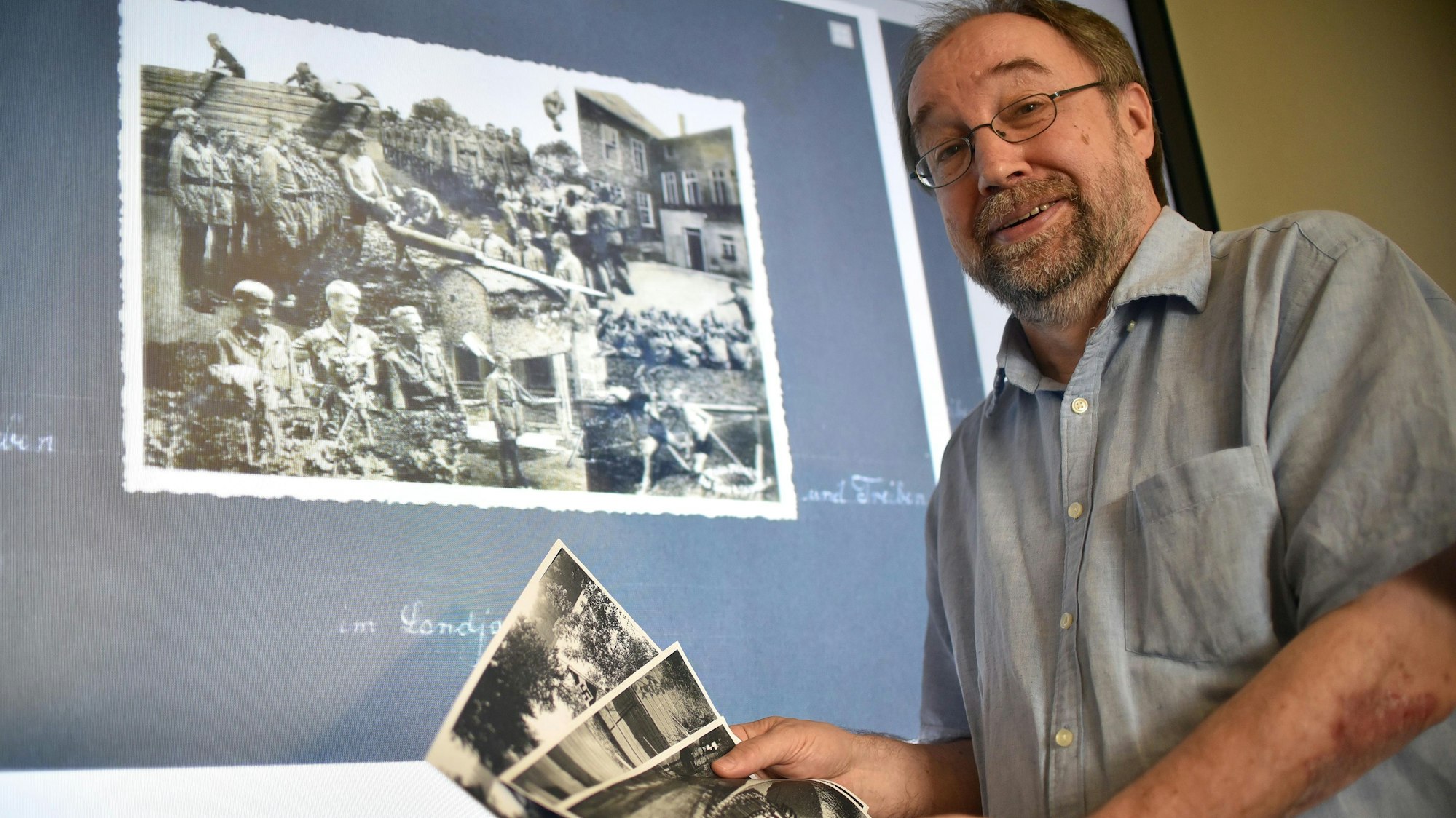 Ein Mann stellt vor einer Leinwand alte Fotos vor.