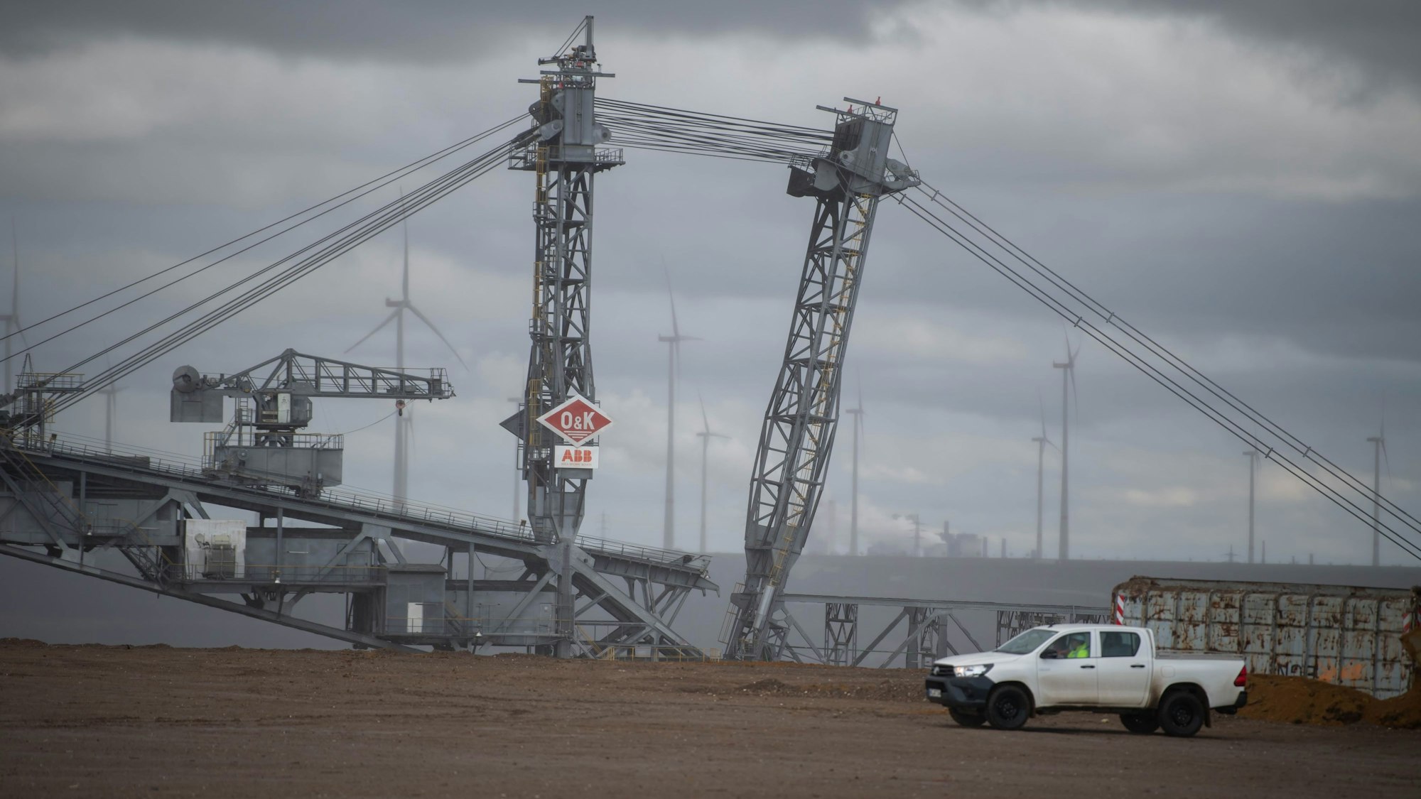 Das Bild zeigt einen Braunkohlebagger in der Nähe des ehemaligen Ortes Lützerath. Im Hintergrund sind Windräder zu erkennen.
