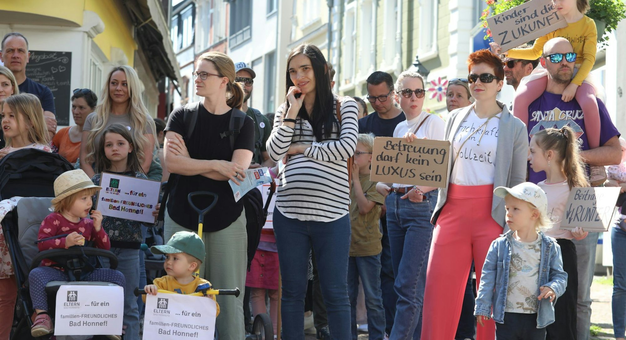 Kinder und ihre Eltern halten Plakate und Schilder in den Händen, auf einem steht „Betreuung darf kein Luxus sein“.