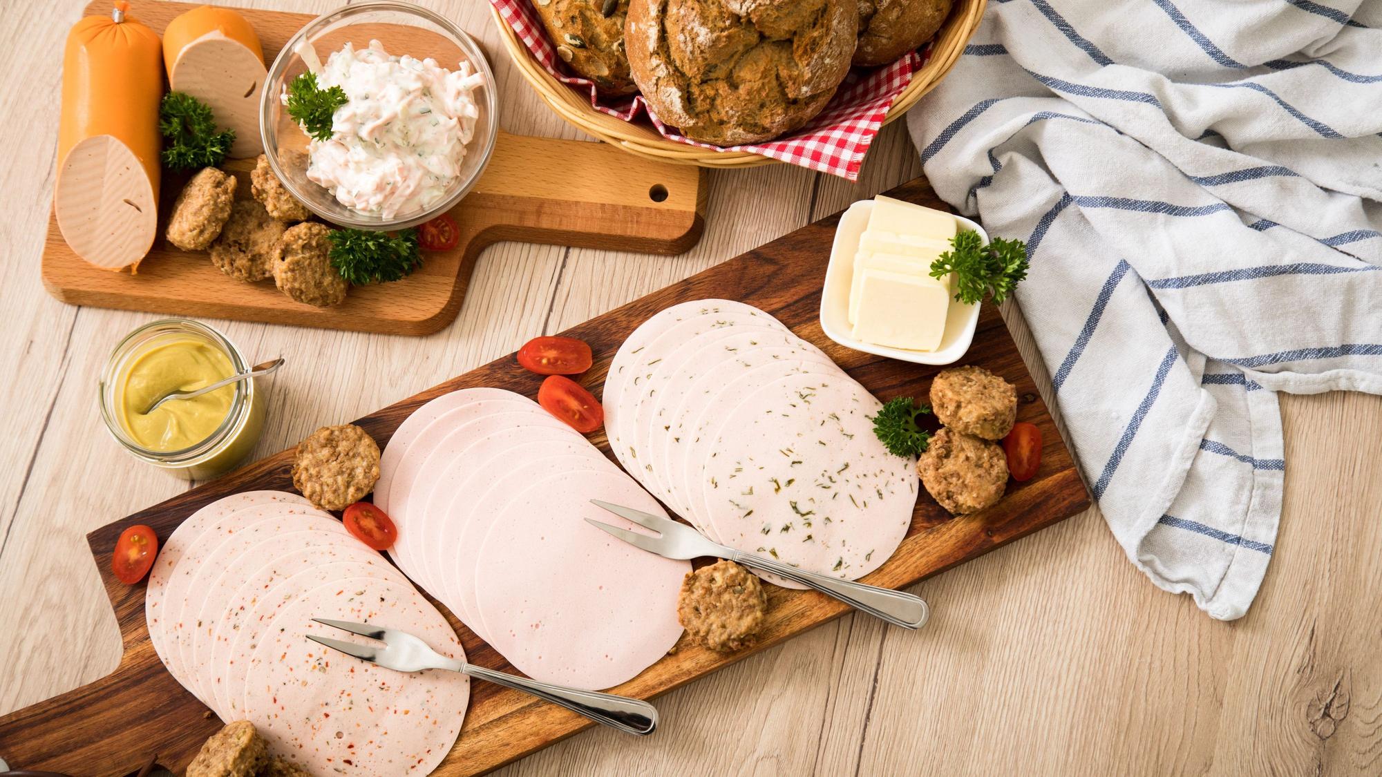 Auf einem Tisch sind vegetarische Salate und vegetarischer Wurstaufschnitt angerichtet.