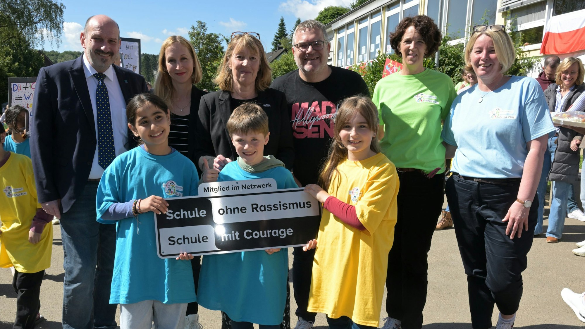 Entertainer Elton steht mit Kindern, Lehrerinnen und Bürgermeister Nicodemus auf dem Schulhof.