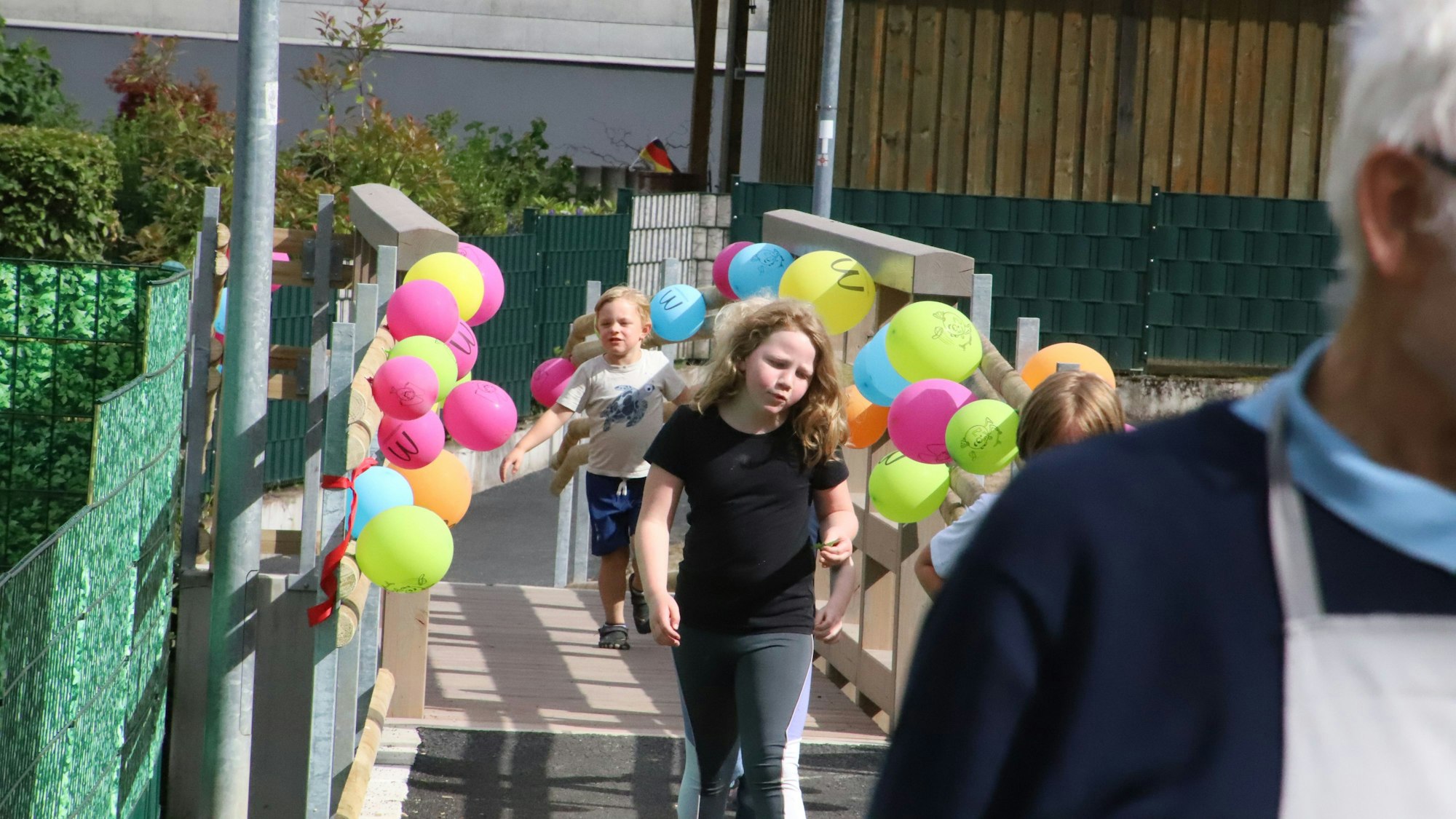 Kinder laufen über eine Brücke, am Geländer hängen zur Eröffnung Luftballons.