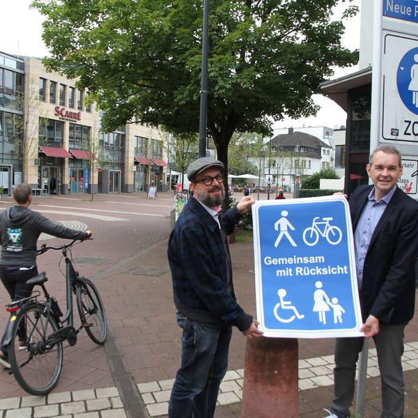 Zwei Männer mit einem blauen Plakat, Aufschrift "Gemeinsam mit Rücksicht"