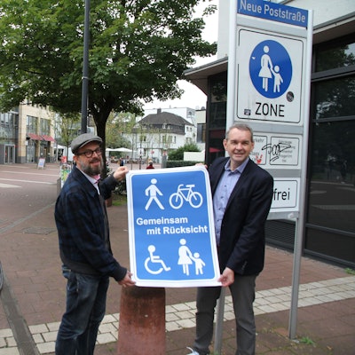 Zwei Männer mit einem blauen Plakat, Aufschrift "Gemeinsam mit Rücksicht"