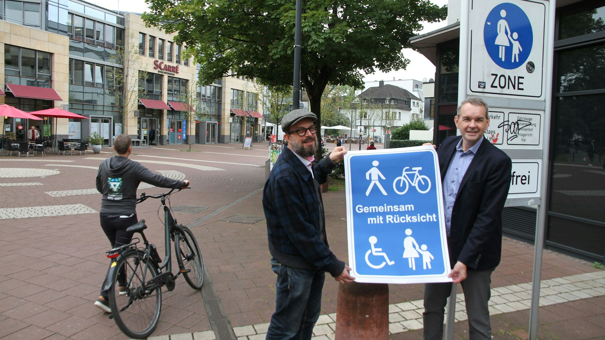 Zwei Männer mit einem blauen Plakat, Aufschrift "Gemeinsam mit Rücksicht"