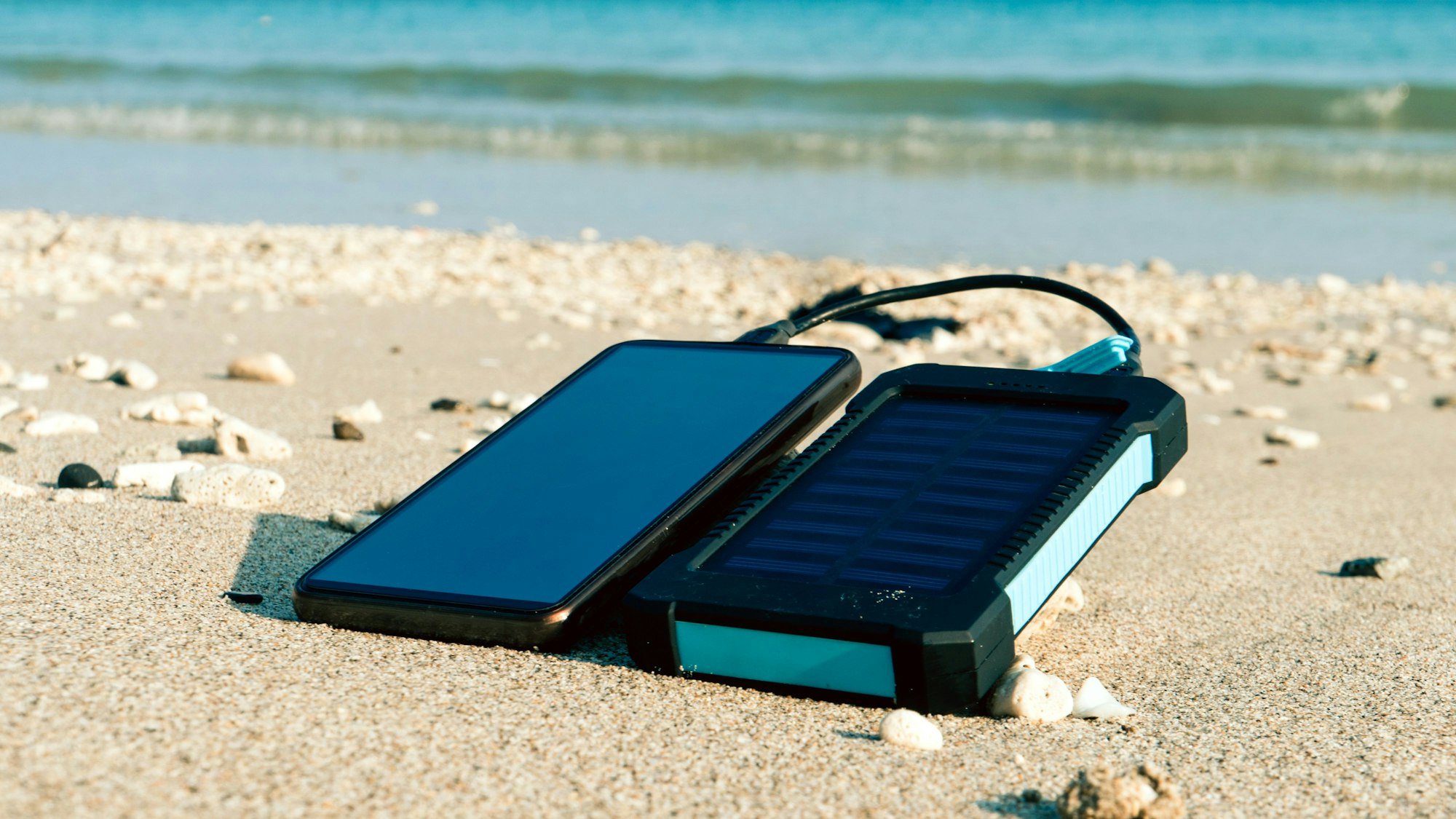 Ein Handy lädt am Strand mithilfe einer solarbetriebenen Powerbank auf