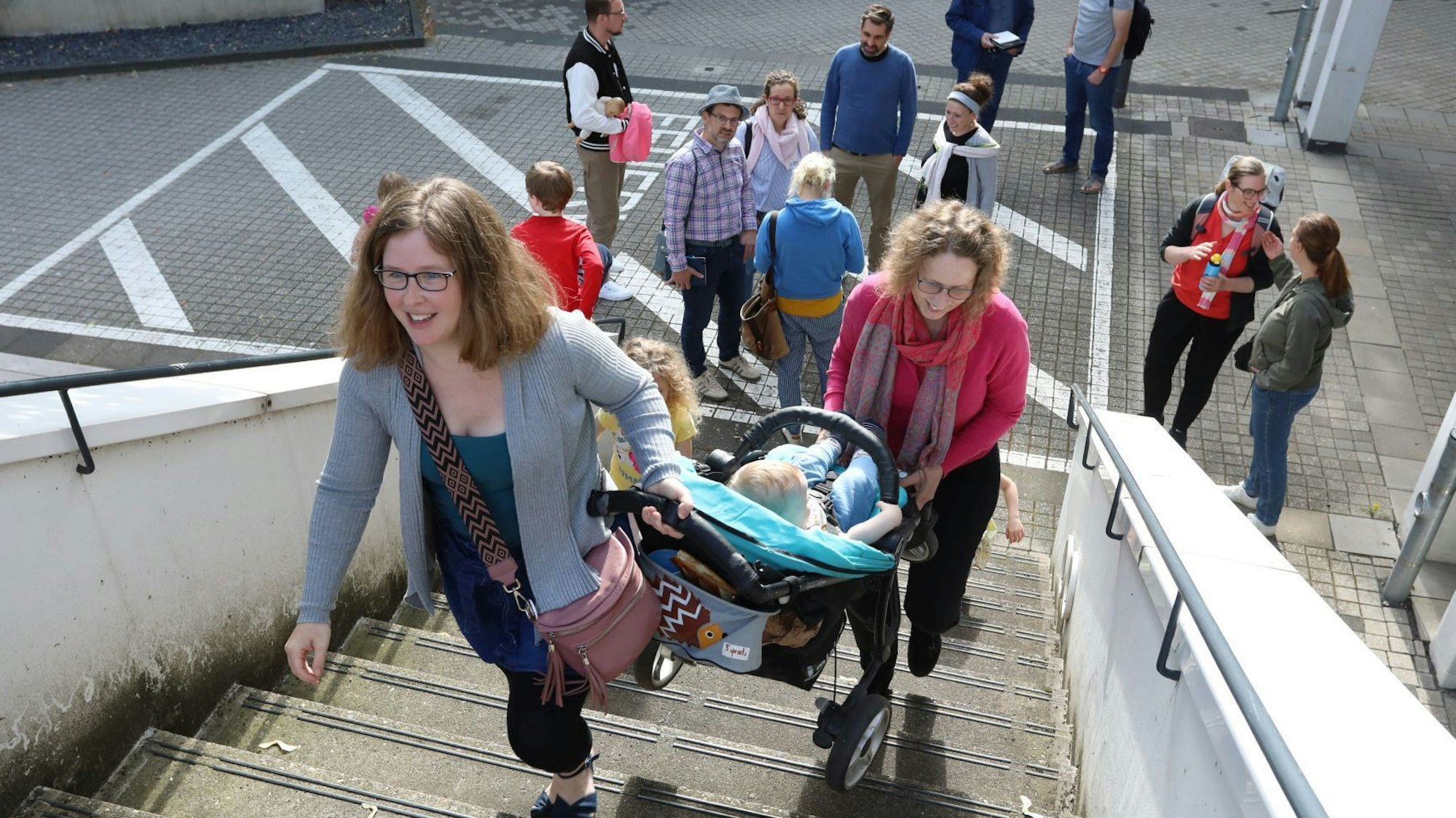 Zwei Frauen tragen einen Kinderwagen die Freitreppe zum Ratssaal im Bad Honnefer Rathaus hinauf.