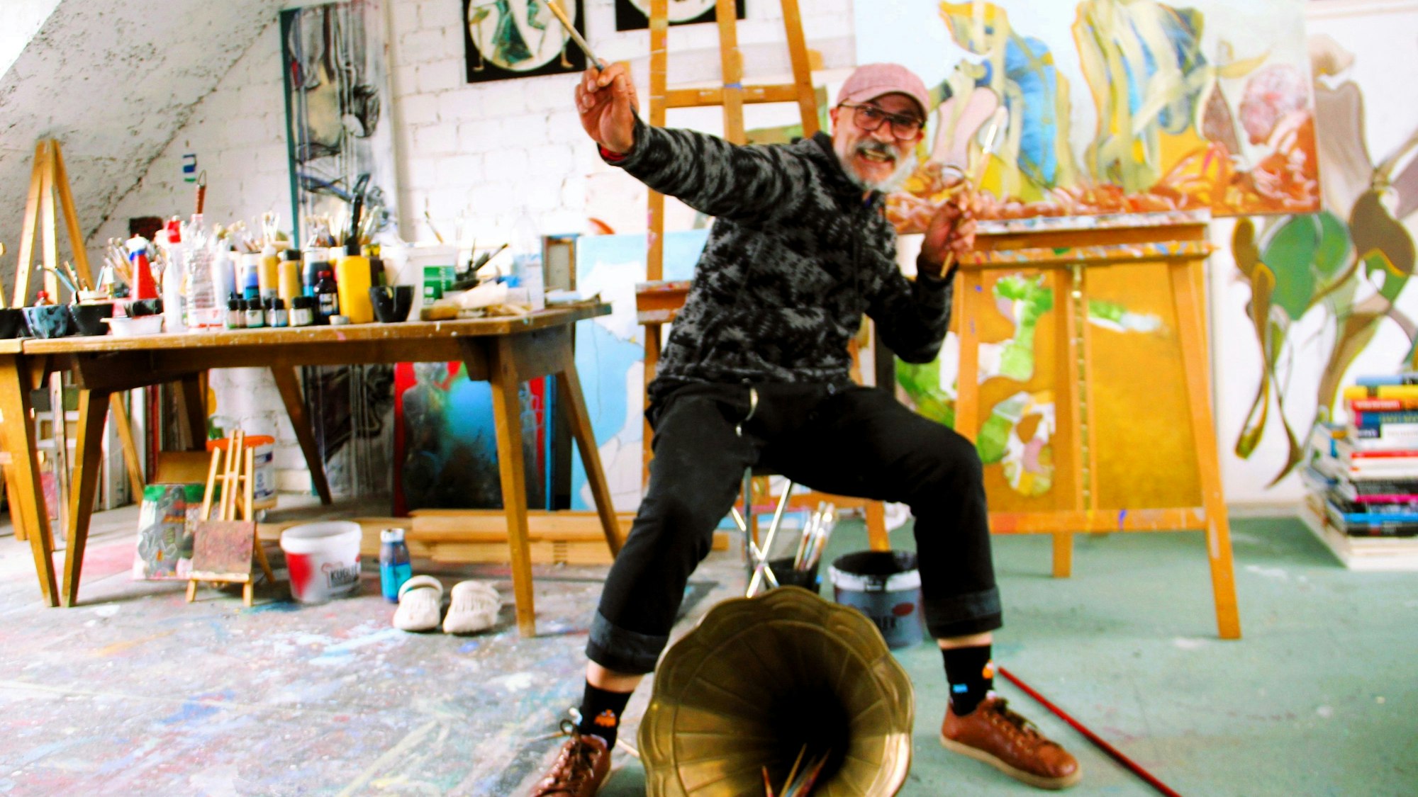 Ein Mann posiert mit einem Pinsel in der Hand in einem Maler-Atelier.