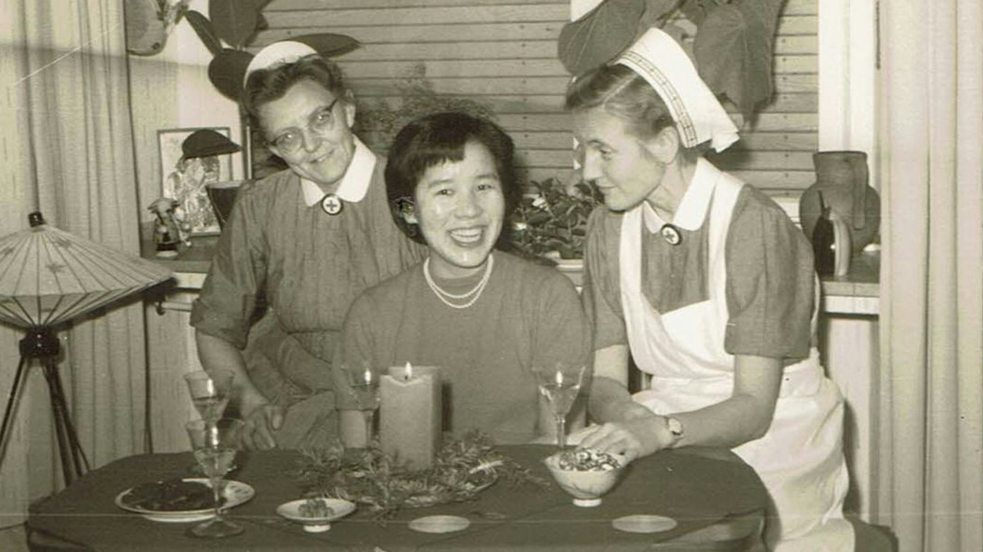 Das Schwarz-weiß-Bild zeigt eine junge Koreanerin mit zwei Rotkreuzschwestern.