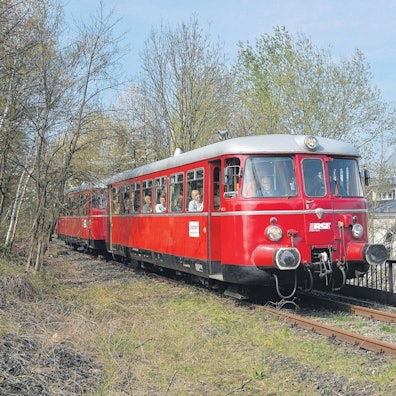 Das Foto zeigt einen Schienenbus auf dem Bahndamm in Höhe der Eisenbahnüberführung Refrather Weg
