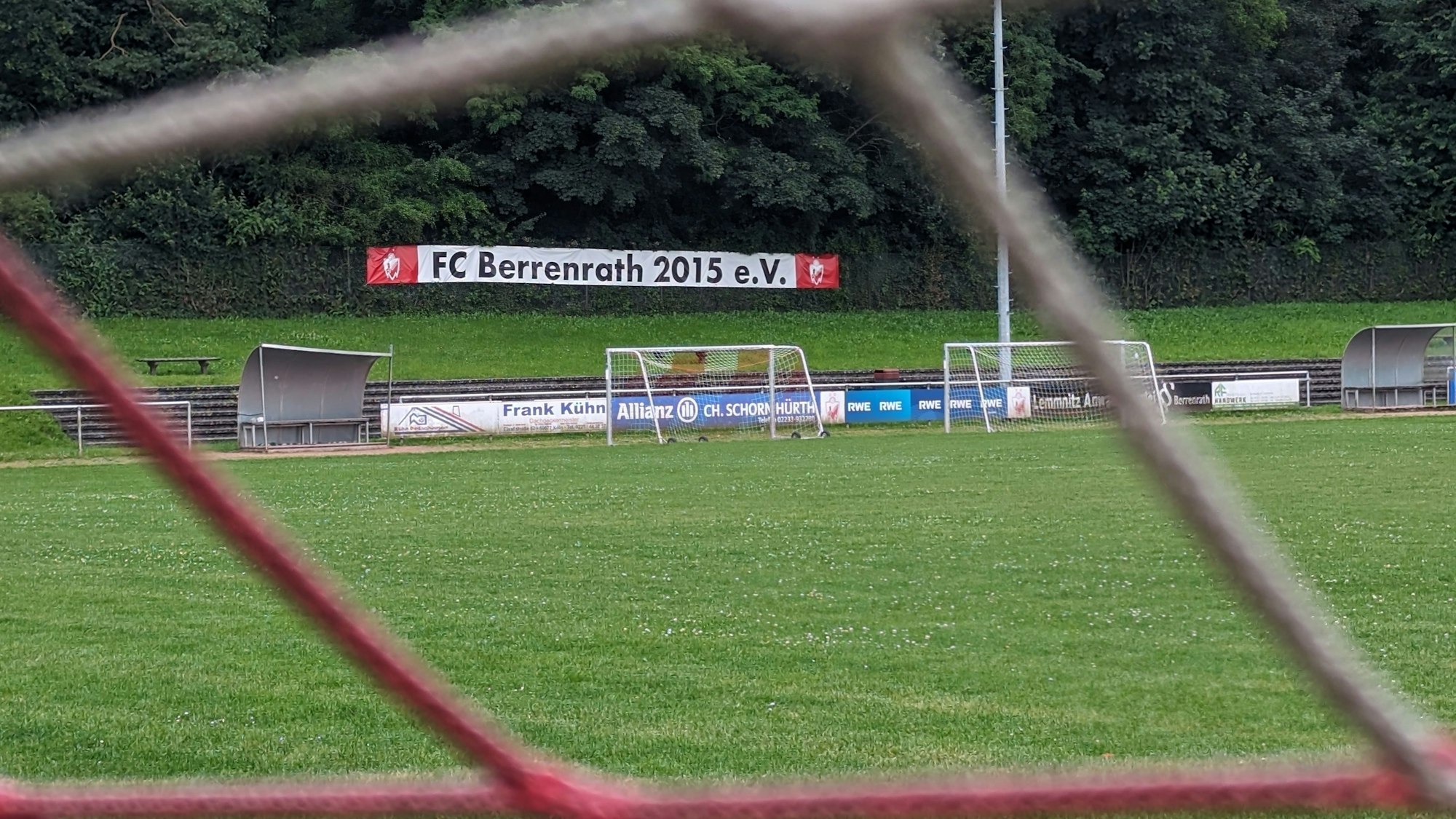 Das Foto zeigt den Naturrasenplatz in Berrenrath hinter den Maschen eines Tornetzes.