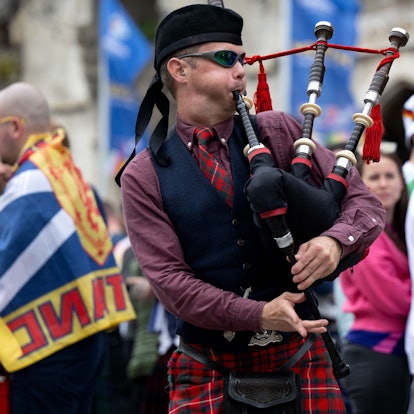Ein schottischer Mann spielt Dudelsack, neben ihm andere Fußballfans mit Trikots und Flaggen.