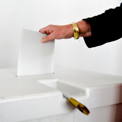 Zu sehen ist, wie eine Person einen Stimmzettel in einer Urne steckt.