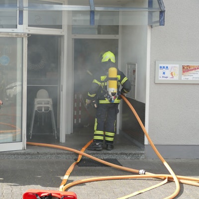 Rauch dringt aus dem Restauranteingang, in dem die Feuerwehrleute stehen.