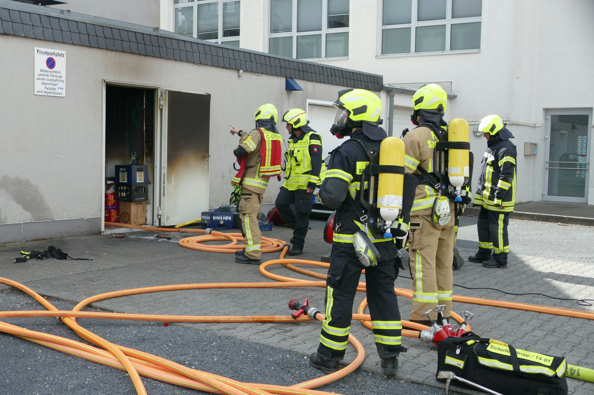 Feuerwehrleute stehen vor einer Hintertür, die schwarz verbrannt ist.