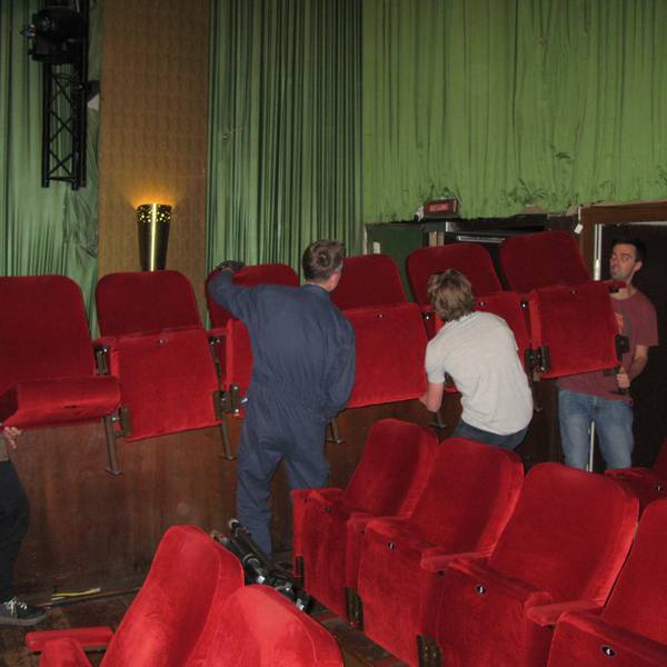 Vier Männer schleppen eine rote Kino-Klappsesselreihe aus dem Kinosaal.