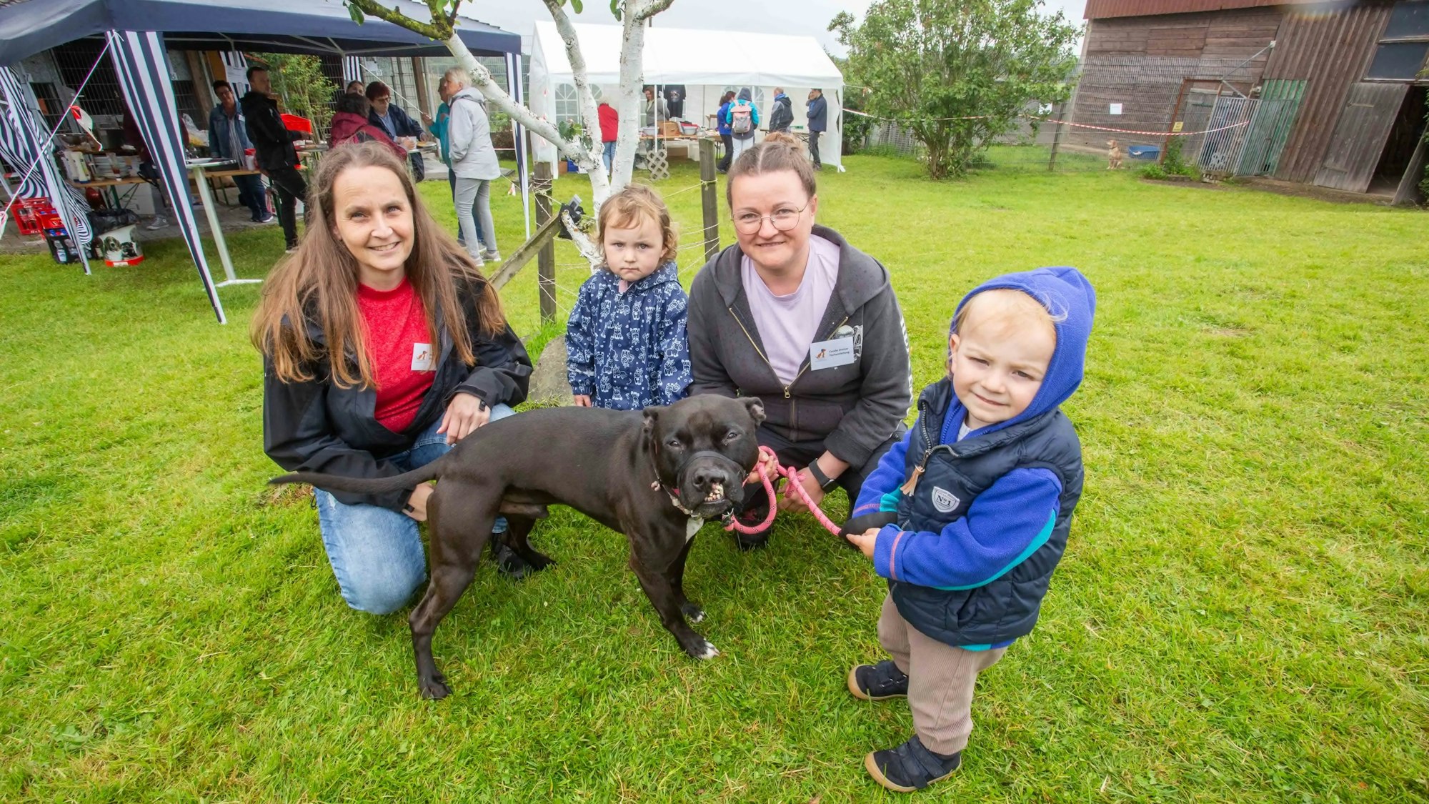 Zwei Frauen und zwei Kinder hocken neben einem Hund.
