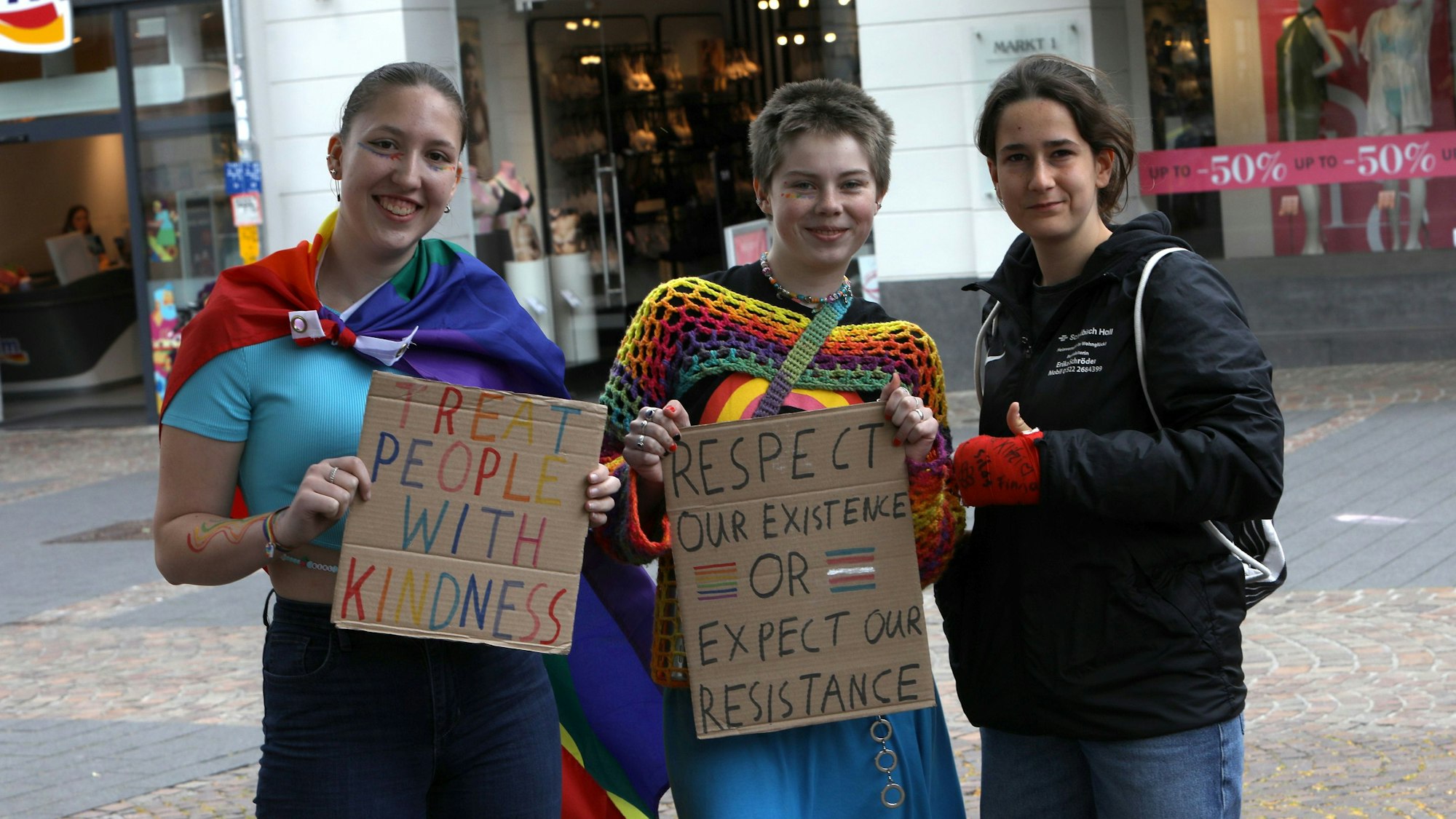 Teilnehmende des Siegburger CSD zeigen Papptafeln mit verschiedenen politischen Aussagen.
