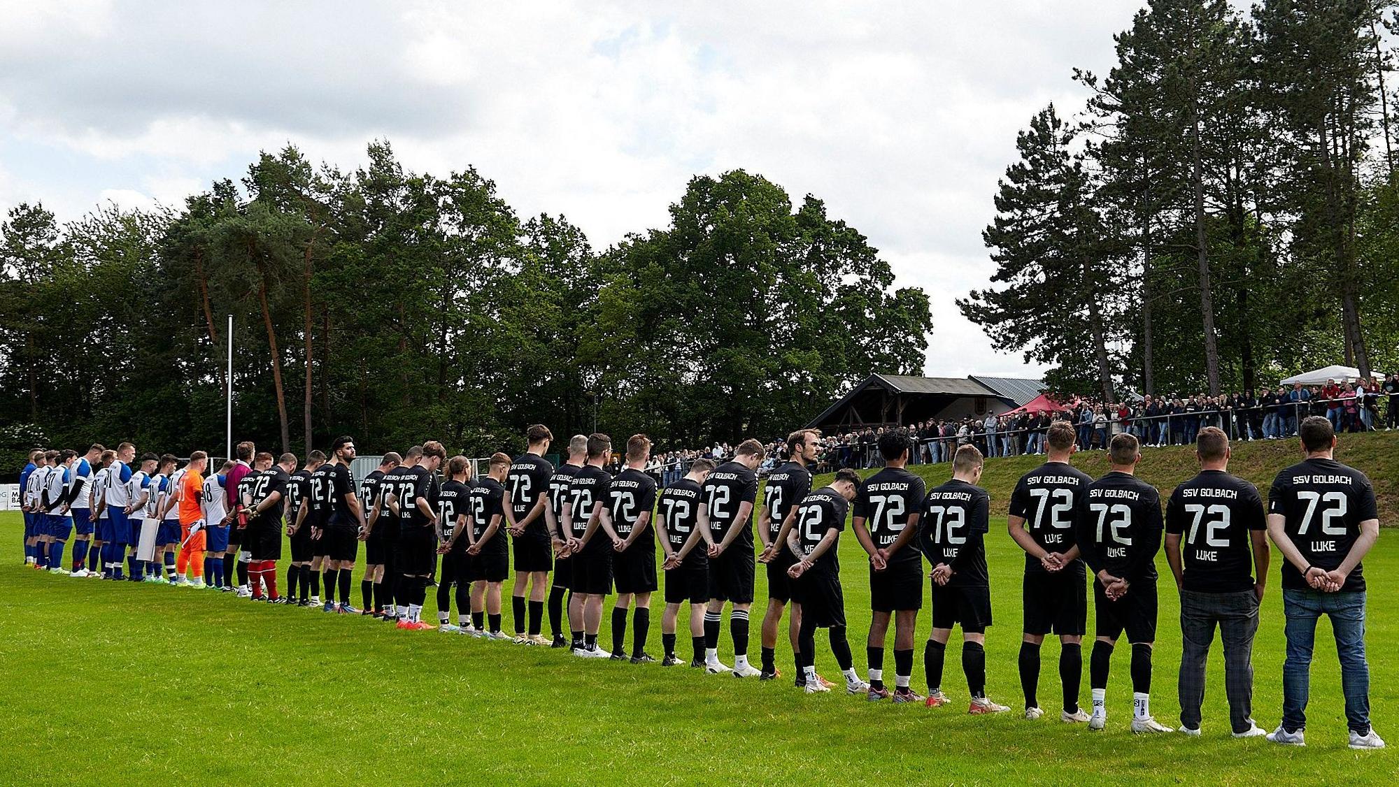 Die Spieler bilden eine Reihe vor dem Publikum. Alle Spieler aus Golbach tragen schwarze Trikots mit der Rückennummer 72.