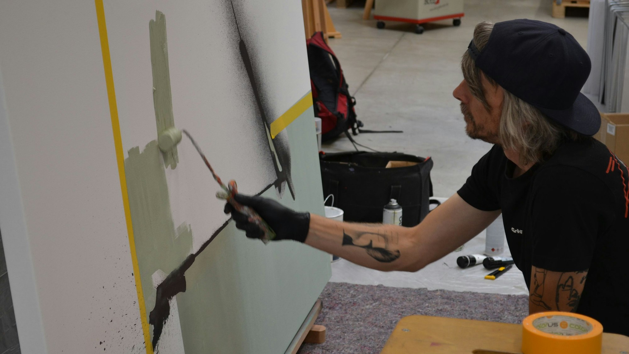 Der Künstler Kai Niederhausen trägt mit einer Rolle Farbe auf eine große Leinwand auf.