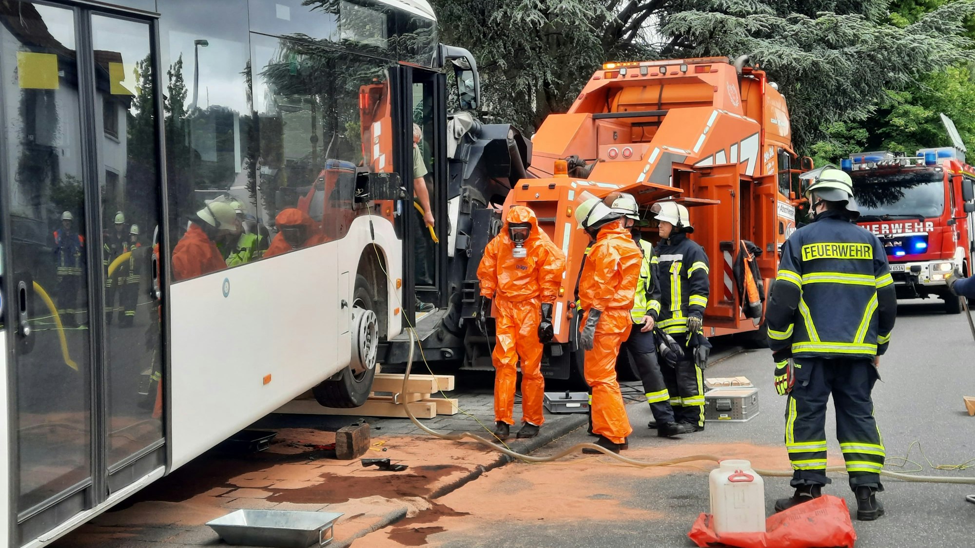 Feuerwehrleute stehen neben einem aufgebockten Bus und tragen orangerote Schutzanzüge.