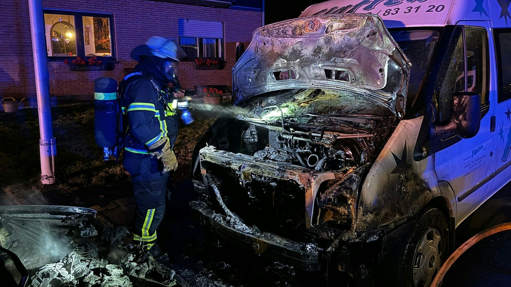 Auf dem Foto leuchtet ein Feuerwehrmann in den Motorraum eines ausgebrannten Sprinters,