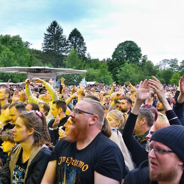 Das Bild zeigt einen Teil der Zuschauer, die stehend das Konzert verfolgen. Einige tragen T-Shirts mit dem Namen der Band.