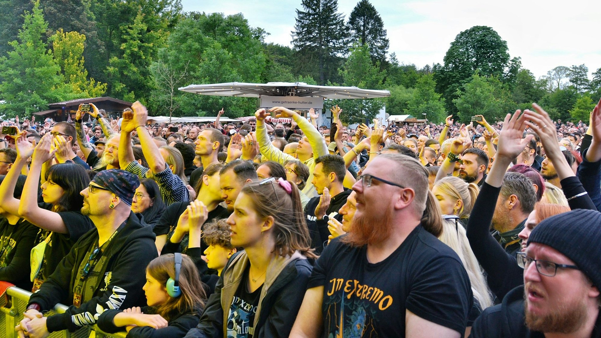 Das Bild zeigt einen Teil der Zuschauer, die stehend das Konzert verfolgen. Einige tragen T-Shirts mit dem Namen der Band.